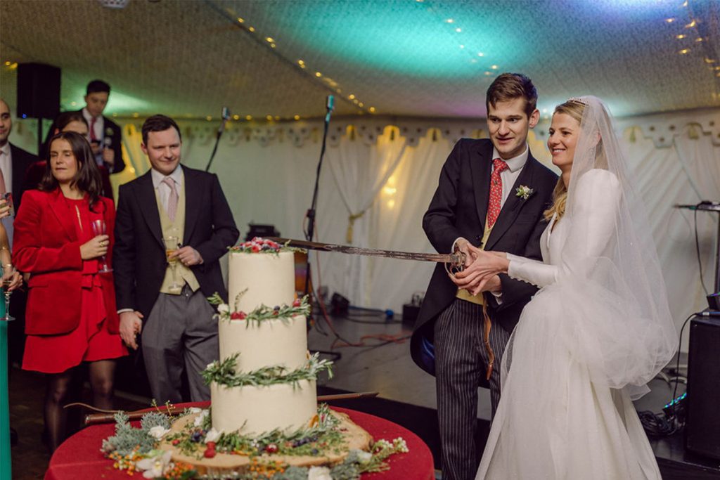Welford Park marquee wedding cutting a wedding cake with a sword