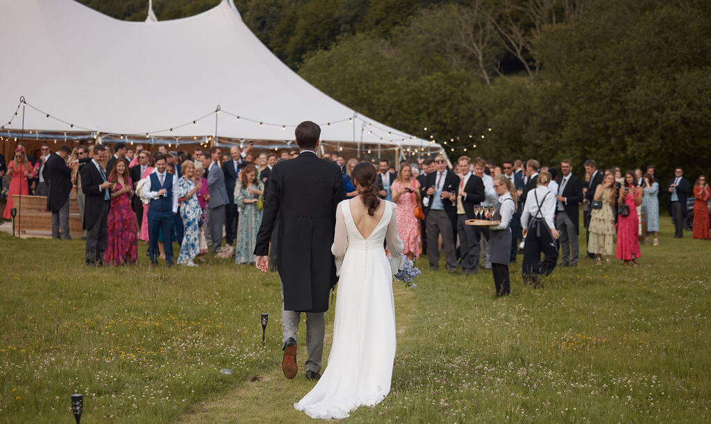 Bride and Groom walking towards a marquee in a a field