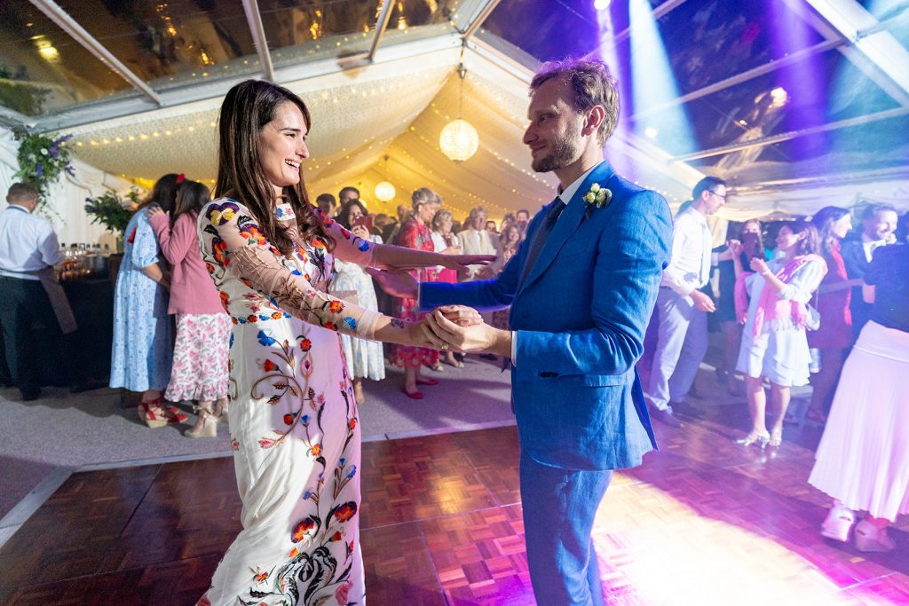 Bride and groom share their first dance in a marquee lit with fairy lights at their Wiltshire garden wedding