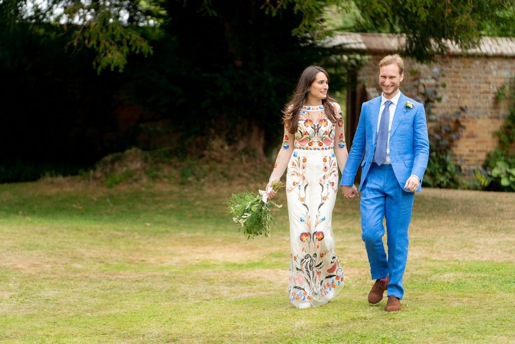 Bride in floral gown and groom in blue suit smiling in Wiltshire countryside following their garden wedding ceremony