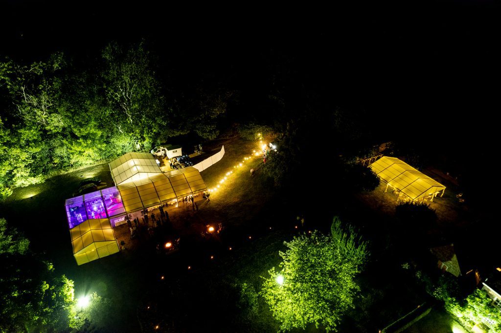 Aerial view of two glowing marquees lit up for a nighttime wedding celebration at a Wiltshire country estate