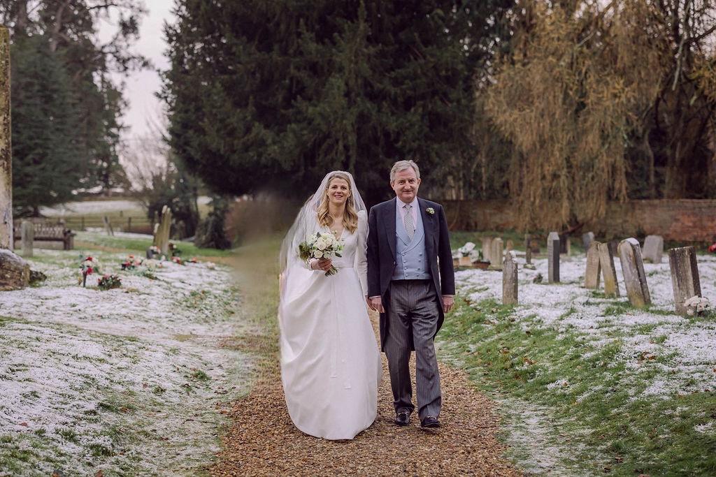 Sassi Holford bride and her father walking to church wedding in snowy Berkshire at Christmas