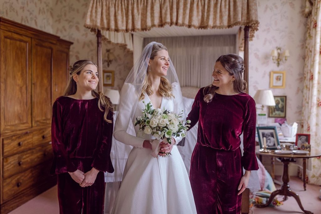 bride with bridesmaids in burgundy standing in front of four poster bed